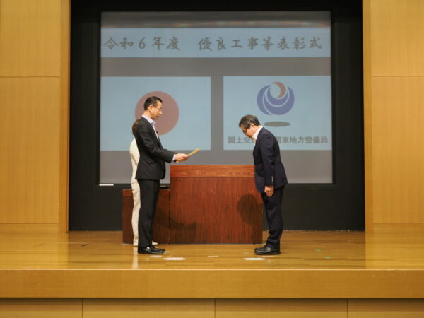 国土交通省受注工事表彰受賞。表彰式の様子。竹花組の代表取締役社長矢野がステージで表彰を受けている様子の画像。
