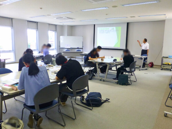 ARIKAMO企業説明中の様子。PowerPointを使って、スクリーン上に映し出して、竹花組の企業の内容説明を８名の諏訪ている学生さん向けにお話をしている様子。