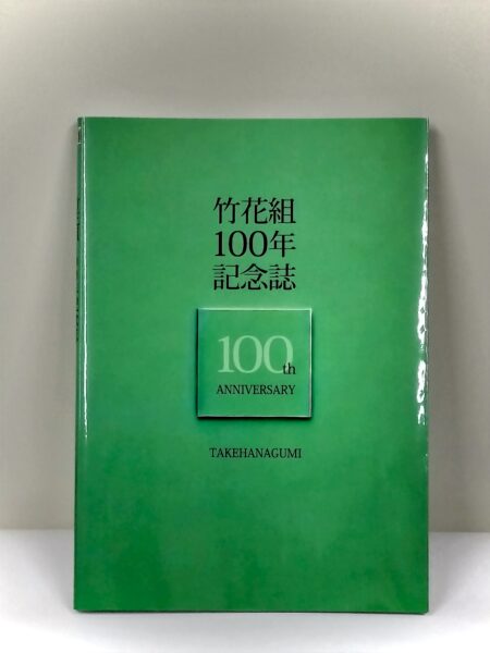 竹花組創業100年を記念して制作された100年記念誌の表紙。全体が光沢がある緑色で真ん中に「１００」のデザインされたマークがある。文字は黒で「竹花組　100年　記念誌」と書かれている。全体的に柄は無くとてもシンプルなデザインの表紙である。