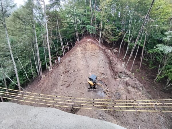令和7年農山漁村地域整備交付金事業 林道妙義荒船線法面改良工事の現場。反対の斜面を登って上から滑車が付いたワイヤーで吊るされているセーフティクライマーの全体像を撮影した画像。