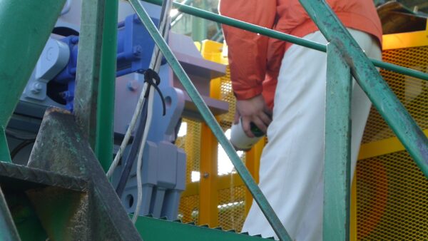 砕石工場の火入れ式にて、お清めのお神酒を機械の周りに巻いている様子の画像