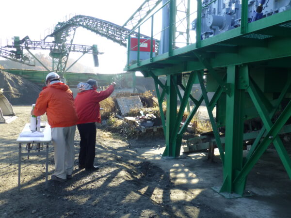 砕石工場の火入れ式にてお清めの塩を新しい機械の周りに巻いている様子の画像。