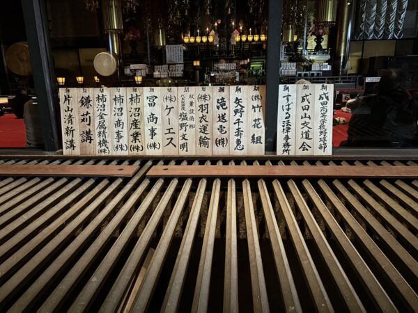 お賽銭箱前に護摩木に祈願をした会社や個人の名前の札が掲げられている画像。竹花組の名前は向かって右から4番目。