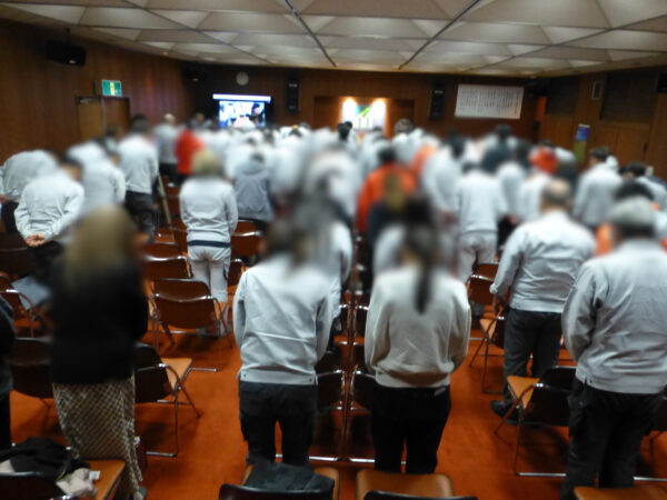仕事納め式開催。開催のあいさつで社員全立ち上がり、お辞儀をしている様子の画像。