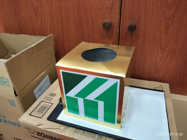 抽選大会の抽選箱。箱全体がゴールドで、前面に竹花組の緑色のロゴマークがついている。