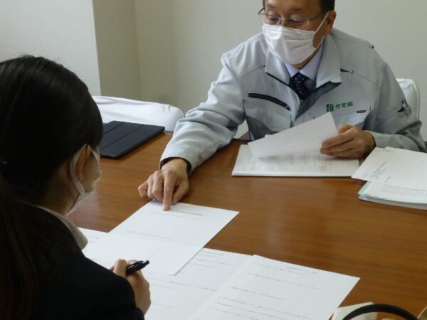 大学生のインターンシップ開催。人事採用業務体験。ワークシートを使った面接官の立場で面談での質問を考える。説明を受けている様子。