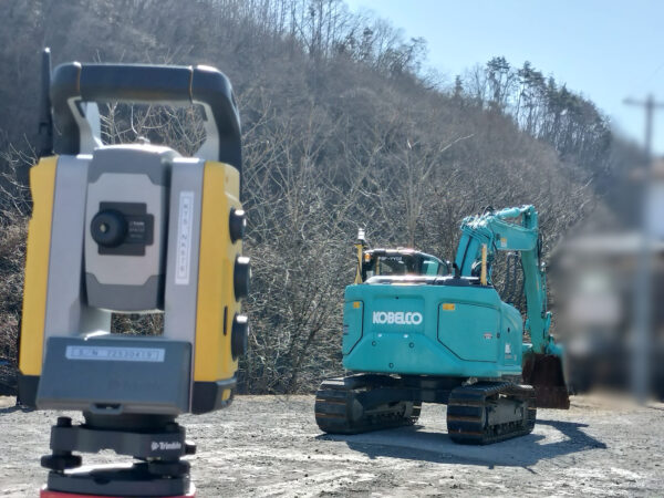 測量機器とバックホウの画像。